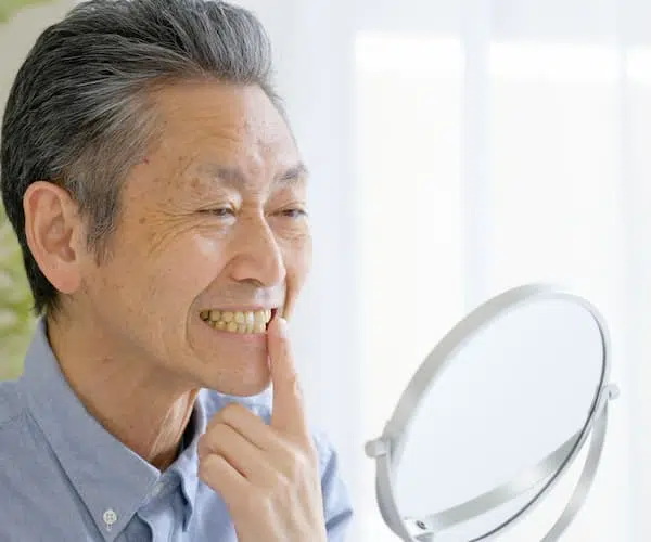 Man examining teeth in mirror, smiling slightly.