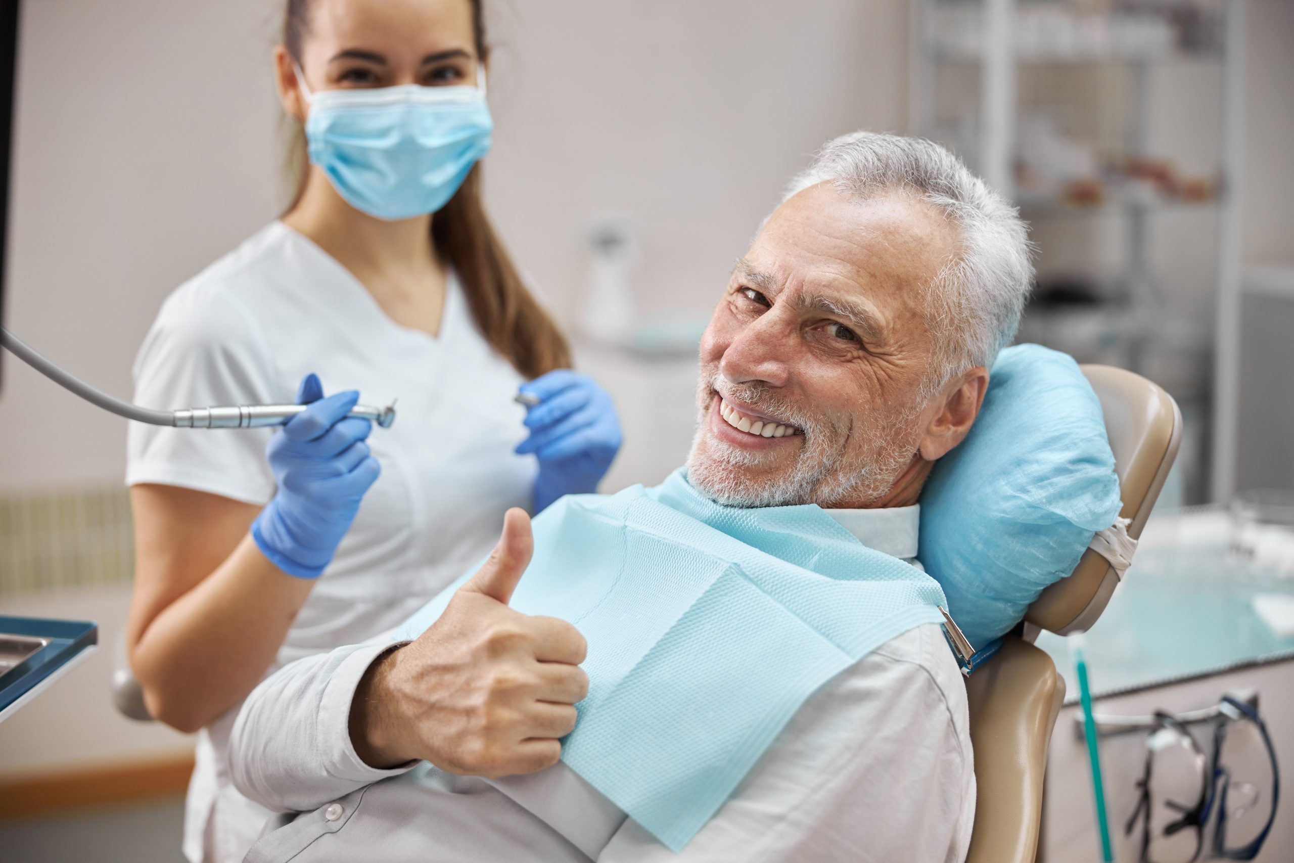 Smiling patient giving thumbs up at dentist office.